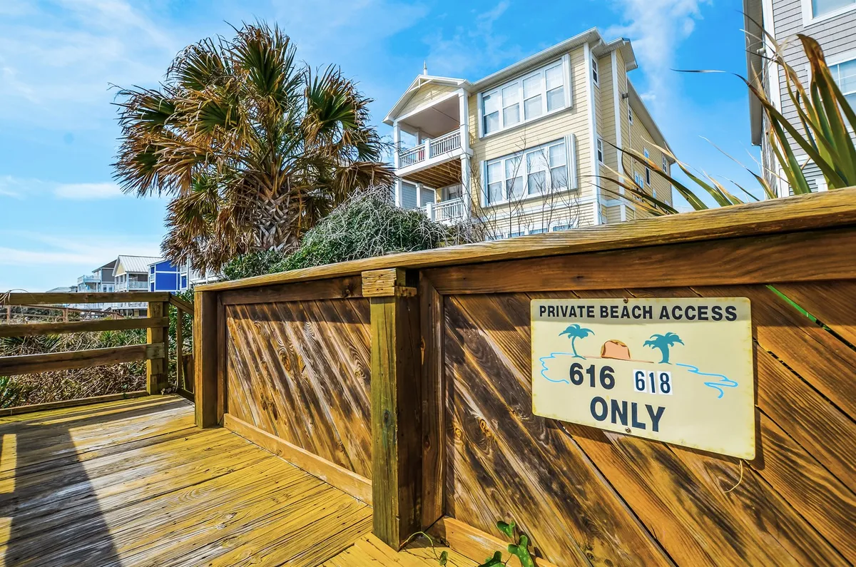 An inviting exterior shot features a private beach access sign, a wooden boardwalk winding through lush palm trees, and the beach visible in the distance. The scene evokes the ease of wandering directly from the property to the shoreline, underscoring the exclusive, accessible nature of the retreat.