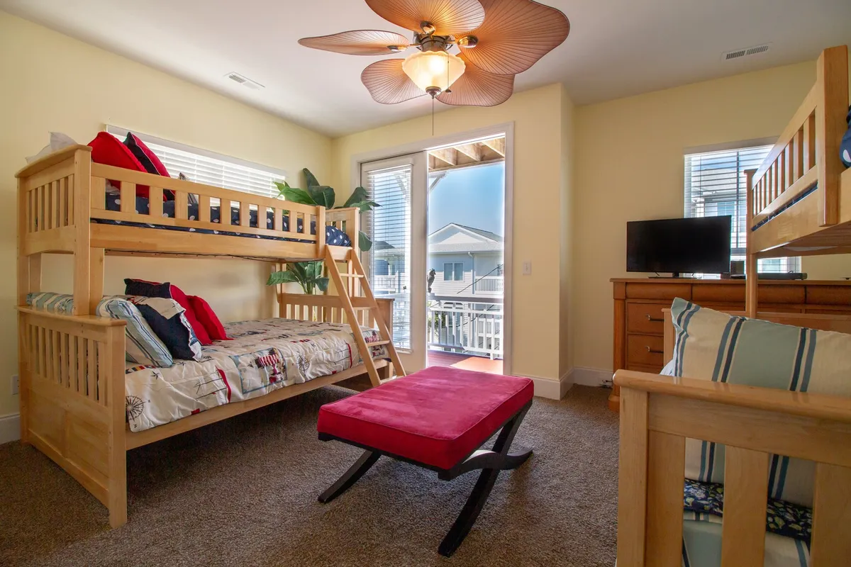 A cheerful bunk room featuring playful bunk beds, a red accent chair, and a large window that lets in ample natural light. The room feels bright and inviting—ideal for kids or family stays.