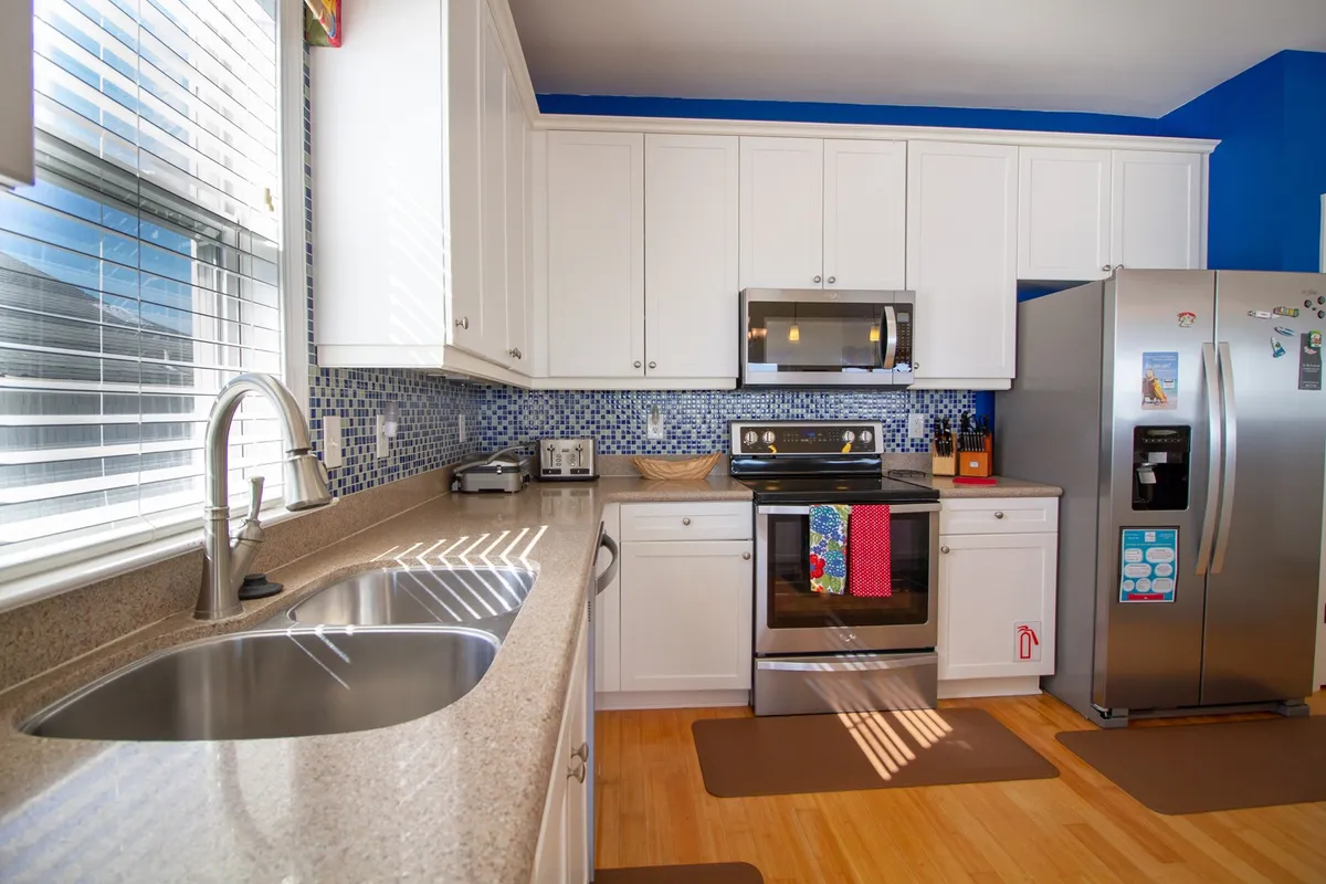 This image showcases a bright, modern kitchen with gleaming stainless steel appliances, colorful dish towels adding a touch of warmth, and a striking mosaic tile backsplash. The countertop provides ample workspace, and the setup is clearly designed for both cooking and socializing.