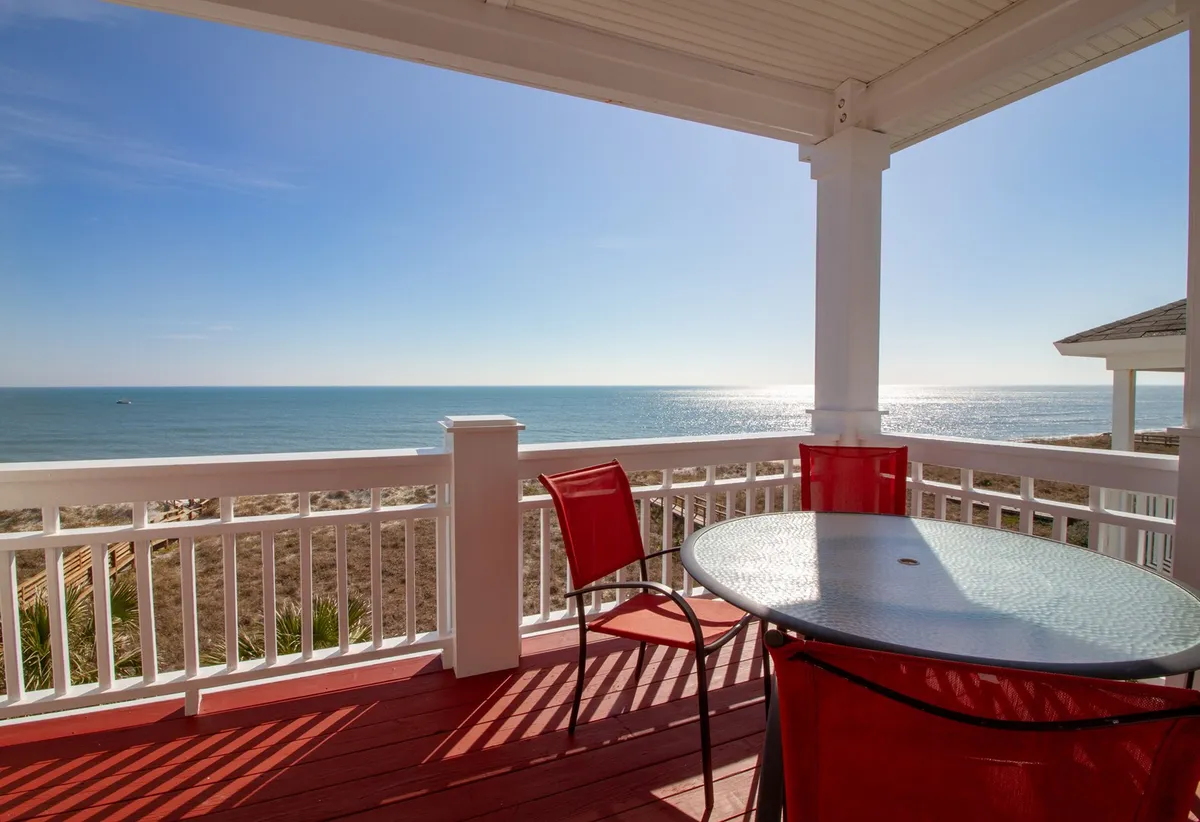 The image features an inviting oceanfront deck with bright red chairs and a glass table, perfectly positioned for relaxing, dining, or enjoying the sunrise over the Atlantic. The peaceful ambiance and panoramic ocean views set the stage for unforgettable moments with family or friends.