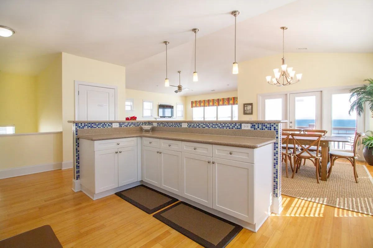 A bright kitchen and dining area with a large kitchen island, a dining table set for gatherings, and expansive windows that let in natural light. The space is stylishly decorated, suggesting both everyday luxury and special occasions.